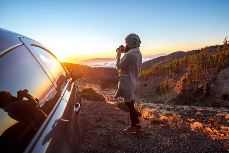 Woman photographing landscape standing near the car